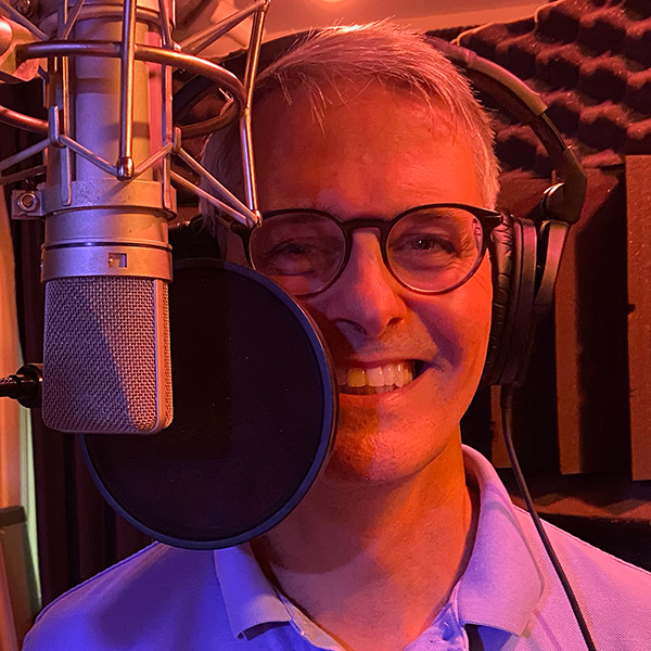 Eric smiling behind a microphone with headphones in a soundbooth